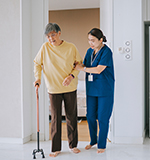 transitional care therapist helping patient walk through kitchen
